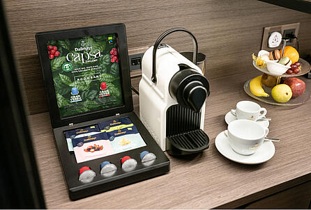 Ochutnávkový box na kapsule a čaj Dallmayr vedľa prístroja na kapsule v hotelovej raňajkovej zóne