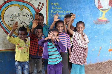 Copii etiopieni râzând stau în fața unui perete colorat și fac cu mâna
