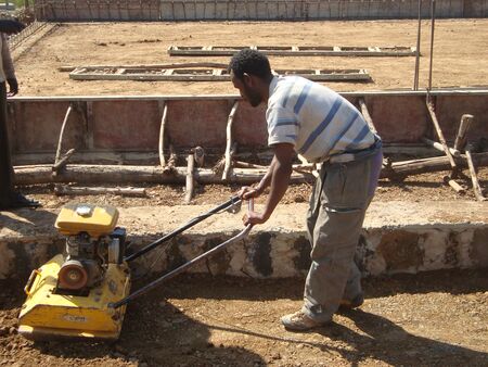 Etiopski pracownik zagęszcza grunt placu budowy szkoły