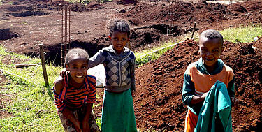 Trei copii etiopieni în fața șantierului școlii