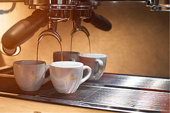Espresso flowing from a portafilter espresso machine into two white espresso cups