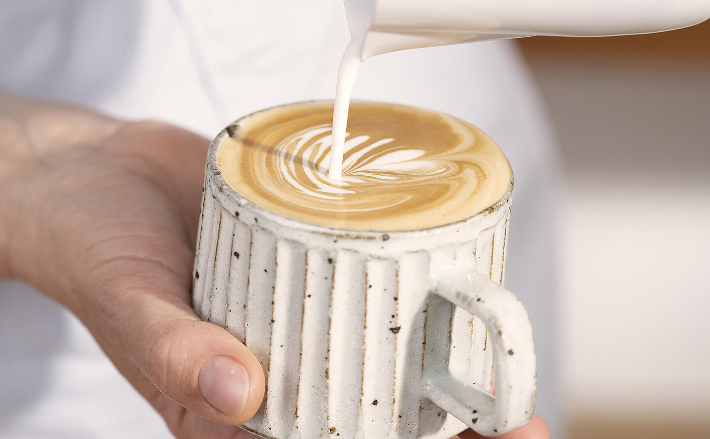 A barista pouring a latte-art heart into a cappuccino cup