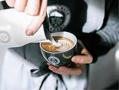 A barista creating latte art in a cappuccino cup