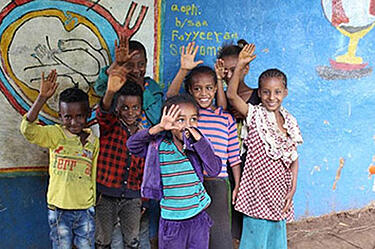 Śmiejące się etiopskie dzieci stoją przed kolorową ścianą i machają