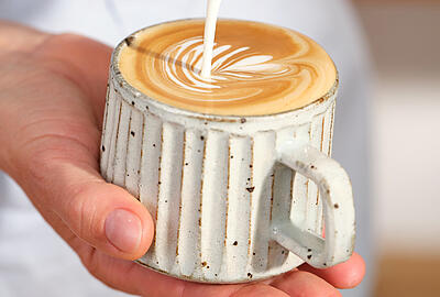 Barista gießt Latte Art in eine rustikale Tasse