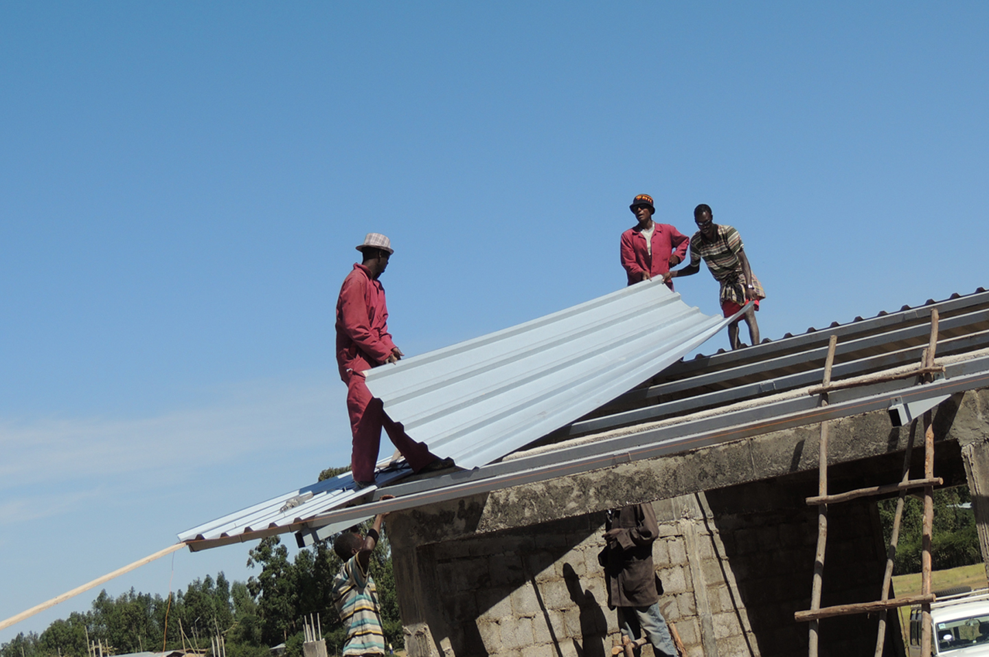 Trzech etiopskich pracowników układa blachy trapezowe na dachu nowej szkoły