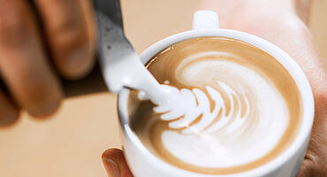 Barista gießt Latte Art in eine Cappuccino Tasse