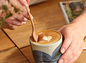 Juodas „Dallmayr“ kapučino puodelis su „Latte Art“ širdimi