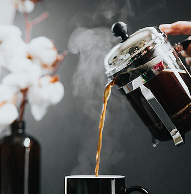 Filter coffee is poured into a cup from a French Press