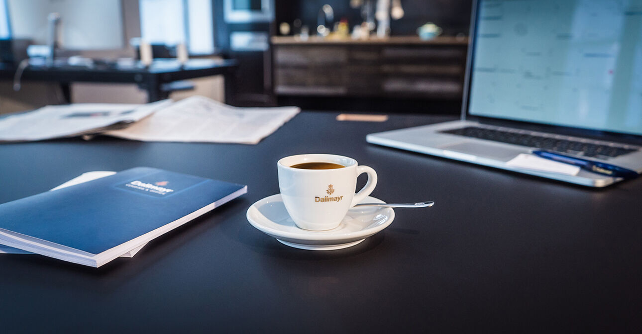 Dallmayr Kaffee Tasse auf Schreibtisch neben Laptop