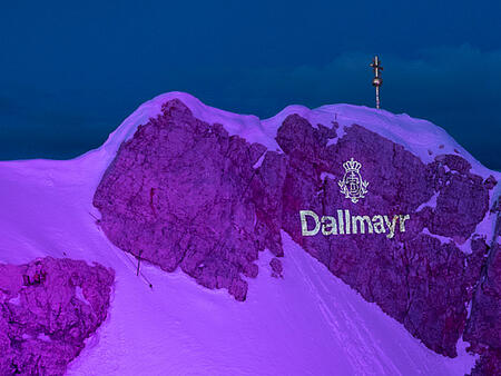 Růžově osvětlená Zugspitze s logem Dallmayr během soutěže Alpenbarista 2019