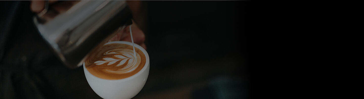 A barista creating latte art in a Dallmayr cappuccino cup
