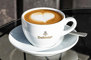 „Dallmayr“ kapučino kava puodelyje su latte menišku širdies motyvu bei maitinimo įstaigoms skirtais reikmenimis