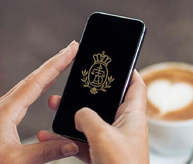 Zwei Hände halten ein Smartphone über einem Dallmayr Cappuccino