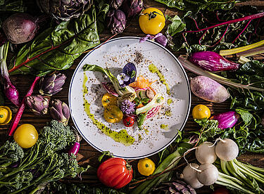 Sommerlich angerichtetes Gericht auf weißem Teller mit Blumen und Gemüse