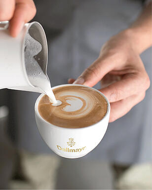 Een barista van Dallmayr giet latte art in een cappuccino
