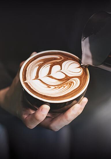 Barista giesst Latte Art in einen Dallmayr Cappuccino