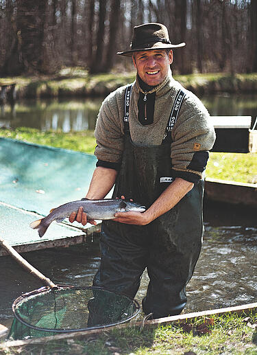 Mann hält frisch gefangenen Fisch aus Wasserbecken in den Händen