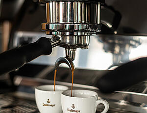 Freshly brewed espresso flowing from a portafilter espresso machine into Dallmayr espresso cups