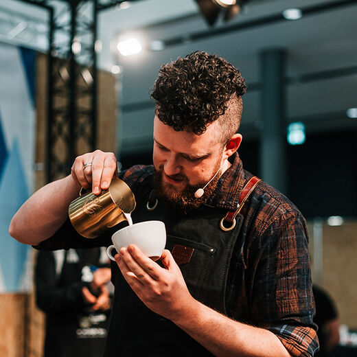 Barista Carlo Graf Bülow gießt Latte Art in einen Cappuccino