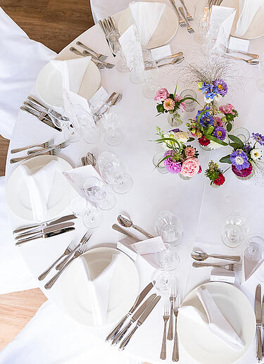 Weiß gedeckter Tisch mit Blumendekoration in hellrosa, lila und rot