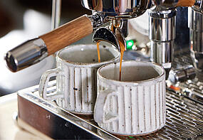 Zwei Espressi fließen aus der Siebträgermaschine in Cappuccino Tassen