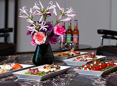 Rosa-lilaner Blumenstrauß auf Tisch mit Vorspeise-Platten
