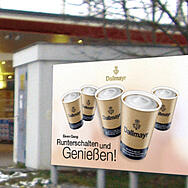 Panou publicitar reprezentând cafea Dallmayr to go într-o benzinărie