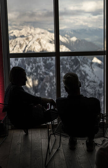 Zwei Gäste des Dallmayr Alpenbarista genießen die Aussicht des Bergpanoramas