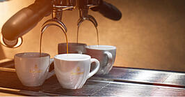 Espresso flows from a portafilter espresso machine into two espresso cups