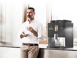 Mann trinkt Dallmayr Kaffee aus Kaffeevollautomaten