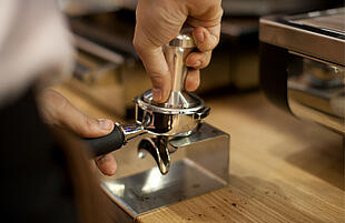 A barista compressing ground coffee in a portafilter with a tamper