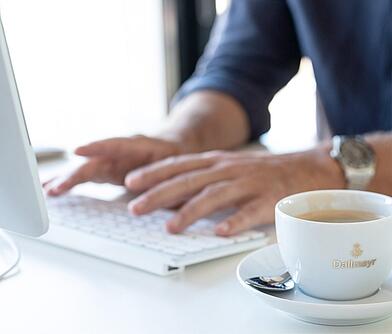 Zwei Hände auf einer Laptoptastatur mit einer Tasse Kaffee