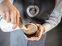 Dallmayr Academy Barista gießt Latte Art in einen Cappuccino