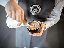 Dallmayr Academy Barista gießt Latte Art in einen Cappuccino