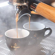 Dallmayri espresso voolab toitlustajatele mõeldud käpaga kohvimasinast kahte musta espressotassi