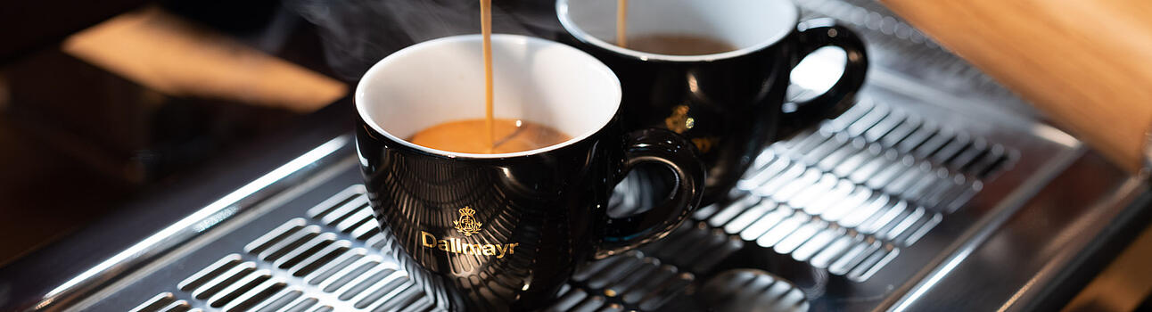 Dallmayr espresso flowing into two black espresso cups from a portafilter espresso machine for food-service