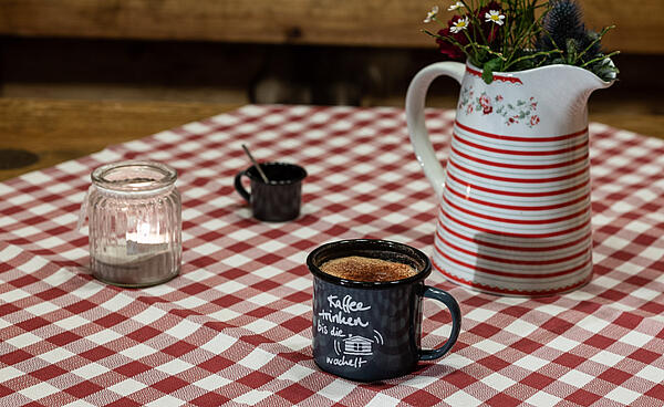 Dallmayr-koffie in emaillen kopje naast bloemenvaas op rood en wit geruit tafelkleed