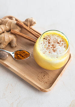 Turmeric latte in a glass, arranged on a tray with ginger and cinnamon