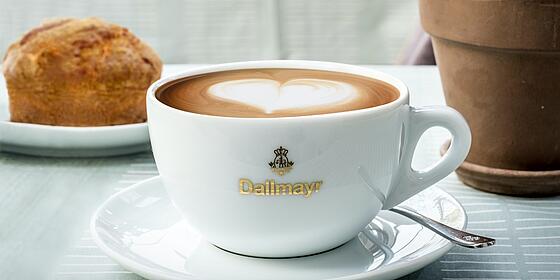 A cappuccino with a latte-art heart in a white Dallmayr cup