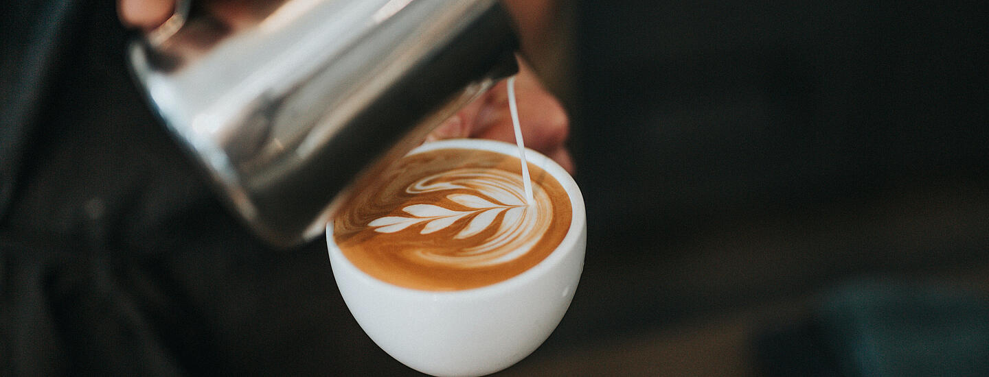 Barista wlewa Latte Art do filiżanki cappuccino Dallmayr
