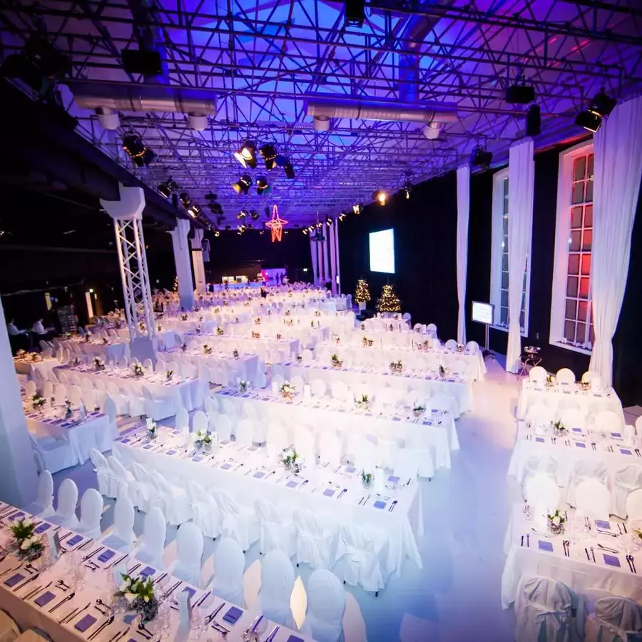 Große Event Location mit weiß gedeckten Tischen, großen Fenstern und heller Beleuchtung