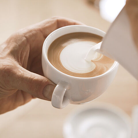 Barista gießt Latte Art in eine Cappuccino Tasse